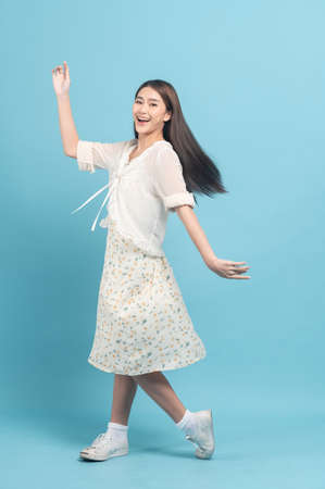 Beautiful young asian woman in white dress with flower pattern feeling surprise isolated on blue backgroundの写真素材