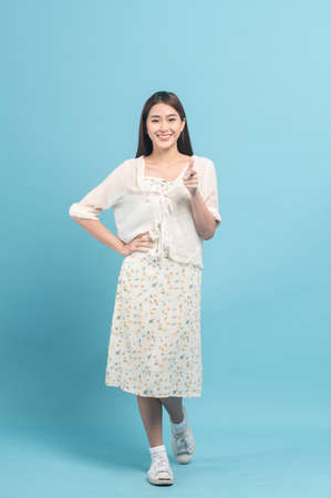 Beautiful young asian woman in white dress with flower pattern isolated on blue backgroundの写真素材