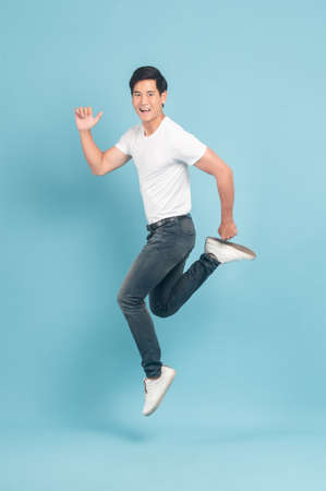 Nice asian guy in white t-shirt and jeans jumping isolated on blue backgroundの写真素材