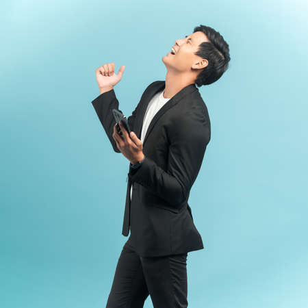 Good looking businessman portrait using smartphone with very excited emotion isolated on blue backgroundの写真素材