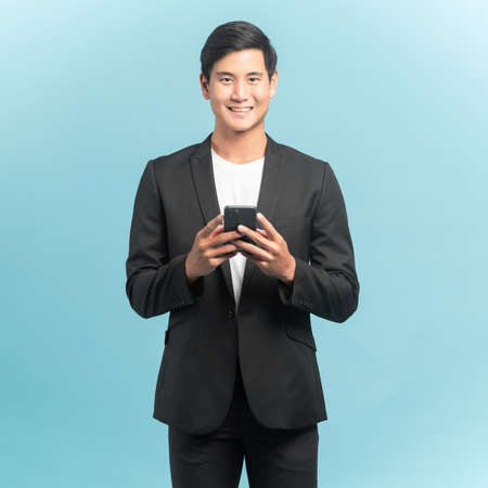 Good looking businessman portrait using smartphone  isolated on blue backgroundの写真素材