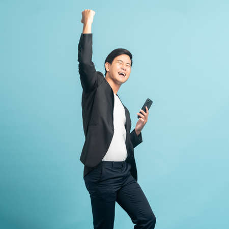Good looking businessman portrait using smartphone with very excited emotion isolated on blue backgroundの写真素材