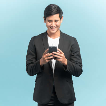 Good looking businessman portrait using smartphone  isolated on blue backgroundの写真素材