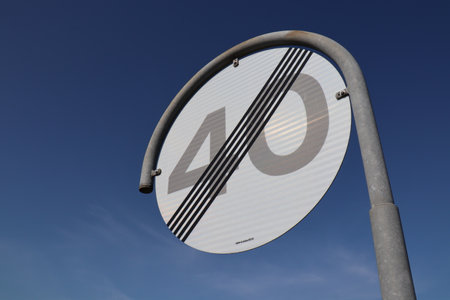 Round traffic sign that cancels speed limit of 40 kph. Grey sign with black lines. Blue sky.