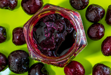 Appetizing cherries jam in glass jar on green apple background