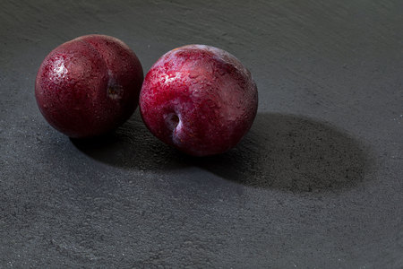 Appetizing and healthy red plums, with a rustic appearance on a black background. Space to insert...