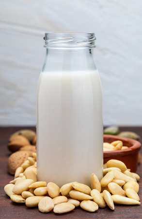 Almond milk in glass bottle. Includes peeled almonds. On rustic wooden background.の写真素材