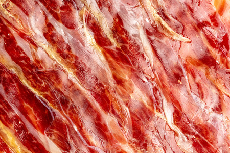 Appetizing slices Iberian ham in the foreground as a texture. Raw meat that becomes an article of haute cuisine and gastronomic luxury, through a process of raw salting and natural curing.の写真素材
