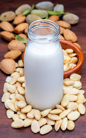 Almond milk in glass bottle. Includes peeled almonds. On rustic wooden background.の写真素材