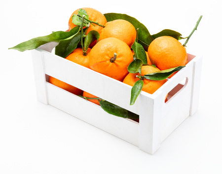 Fresh and raw tangerines with green leaves in wooden box. Isolated on white background.の写真素材