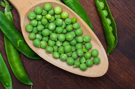 Green, tender, fresh and raw peas. Close-up and top view. Rustic appearance. Rustic appearance and wooden spoon.の写真素材