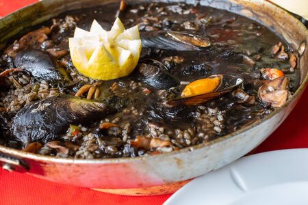 Close-up of black rice with squid â€“in inkâ€“ mussels, clams and other seafood. Presented...