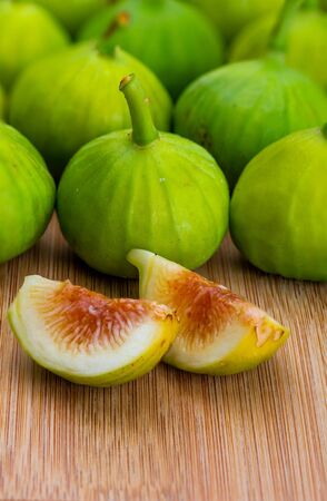 Whole and cut green figs, with fig leaves. Foreground. On wooden background.の写真素材