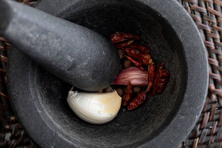 Close up with garlic, black pepper and chilli peppers. In stone mortar. Rustic appearance.の写真素材