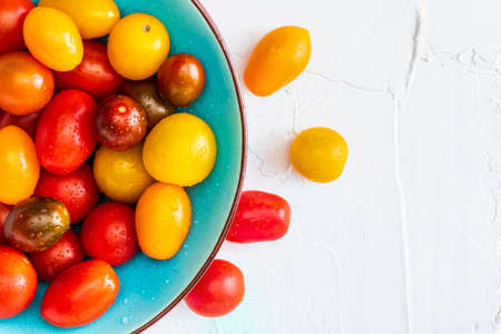 Bowl of colorful cherry tomatoes (red, garnet and yellow), fresh and raw. With water drops On white textured background and space to insert text (copy space). Top Viewの写真素材