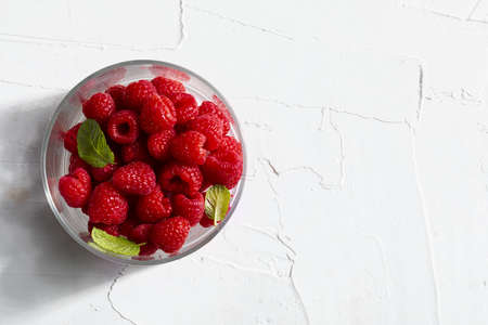 Delicious and appetizing raspberries in a glass bowl and mint leaves (peppermint, mint). On white...