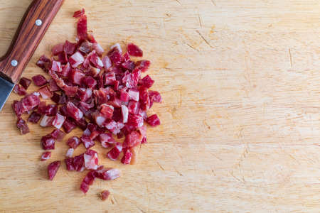 Iberian ham (serrano) cut into cubes (diced). On wooden board with knife. Copy space.の写真素材