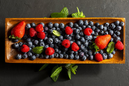 Appetizing variety of forest fruits (strawberries, strawberries, raspberries, blueberries, red berries) on a wooden tray and mint leaves (peppermint, mint). On white textured background. Top view with copy space.の写真素材