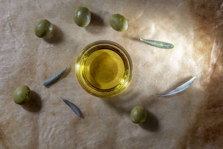Extra virgin olive oil in glass bowl. It includes olive leaves and branches. Rustic Background. Top view.の写真素材