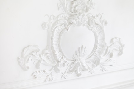 Beautiful ornate white decorative plaster mouldings in studio. The white wall is decorated with exquisite elements of plaster stuccoの写真素材