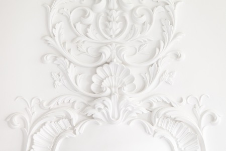 Beautiful ornate white decorative plaster mouldings in studio. The white wall is decorated with exquisite elements of plaster stuccoの写真素材