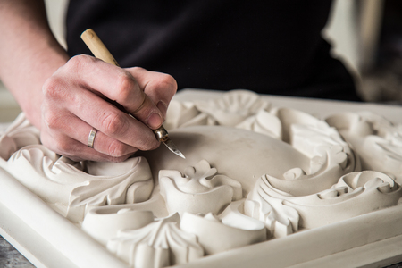 Hands of the sculptor with the tool. The sculptor works in the Studio. Creation of a decorative element from plaster. Luxurious stucco in Baroque style. Close up. Selective focus.の写真素材