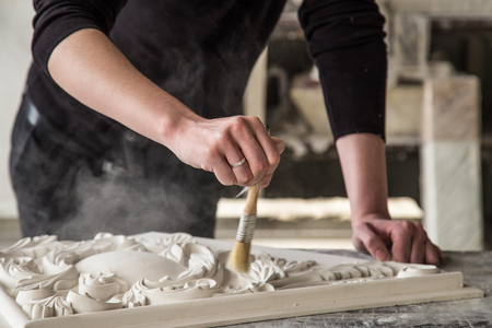 Hands of the sculptor with the tool. The sculptor works in the Studio. Creation of a decorative element from plaster. Luxurious stucco in Baroque style. Close up. Selective focus.の写真素材