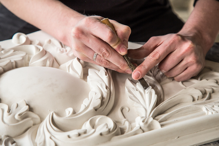 Hands of the sculptor with the tool. The sculptor works in the Studio. Creation of a decorative element from plaster. Luxurious stucco in Baroque style. Close up. Selective focus.の写真素材