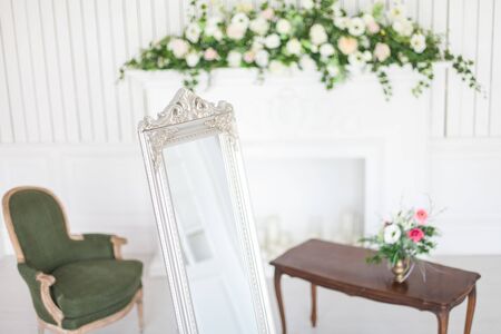 Mirror in classic bright interior with fireplace and armchair. Spring interior decoration with flowers.の写真素材