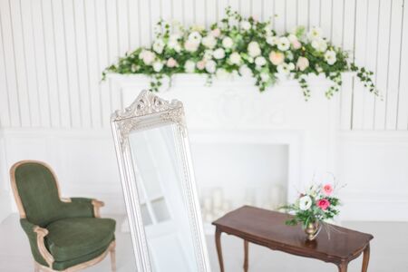 Mirror in classic bright interior with fireplace and armchair. Spring interior decoration with flowers.の写真素材