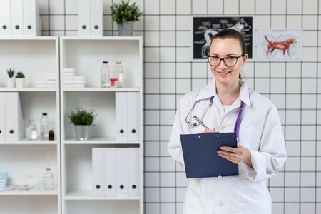 Beautiful woman veterinarian smiling. Veterinary clinic. Holding a tablet and a pen.の写真素材