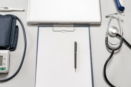 Stethoscope, measuring blood pressure and laptop on wooden desk for analysis of medical results.の写真素材