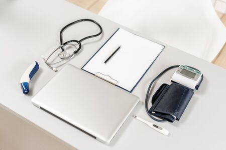 Stethoscope, measuring blood pressure and laptop on wooden desk for analysis of medical results.の写真素材