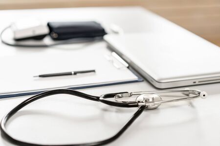 Stethoscope, measuring blood pressure and laptop on wooden desk for analysis of medical results.の写真素材