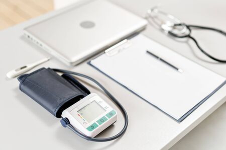 Workplace of doctor with laptop, stethoscope and notebook on wooden table in the office. Blood Pressure Monitor. Medical equipment. Cardiac diagnosis. vintage tone.の写真素材