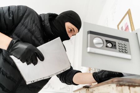 The thief opens the electronic safe. The burglar commits a crime in Luxury apartment with stucco. Thief with black balaclava stealing safe box.の写真素材