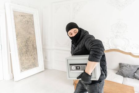 Thief with black balaclava stealing modern Electronic safe box. The burglar commits a crime in Luxury apartment with stucco.の写真素材