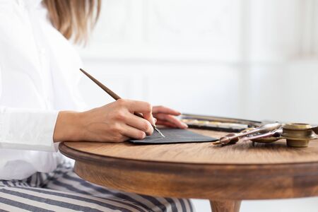 Woman calligrapher is holding a pen with ink and signs a card in handwritten font. Close-up. Soft focus.の写真素材