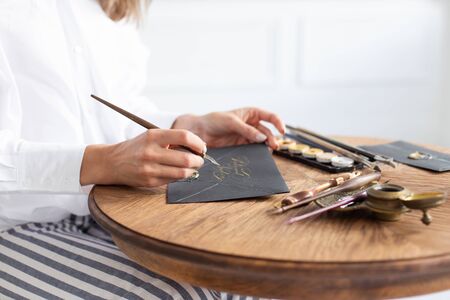 Woman calligrapher is holding a pen with ink and signs a card in handwritten font. Close-up. Soft focus.の写真素材
