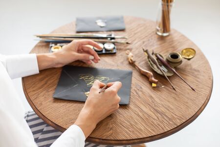 Woman calligrapher is holding a pen with ink and signs a card in handwritten font. Close-up. Soft focus.の写真素材