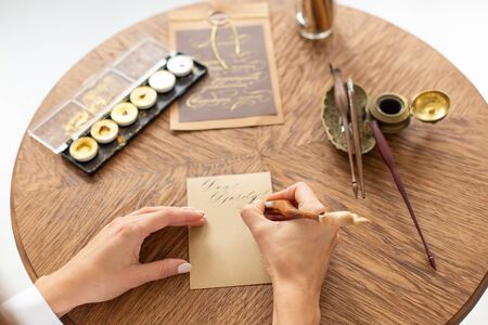 Calligrapher is holding a pen with ink. The girl writes a letter in handwritten font. Creative workshop of the artist. Soft focus.の写真素材