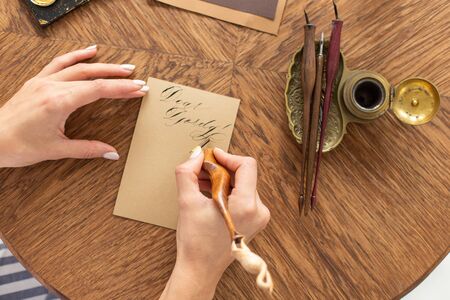 Calligrapher is holding a pen with ink. The girl writes a letter in handwritten font. Creative workshop of the artist. Soft focus.の写真素材