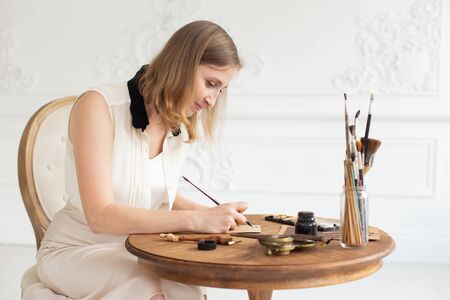 An attractive female artist sits at a table in an art workshop and draws a sketch of a drawing.の写真素材