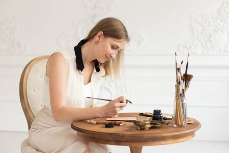 An attractive female artist sits at a table in an art workshop and draws a sketch of a drawing.の写真素材