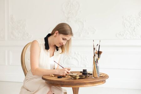 An attractive female artist sits at a table in an art workshop and draws a sketch of a drawing.の写真素材