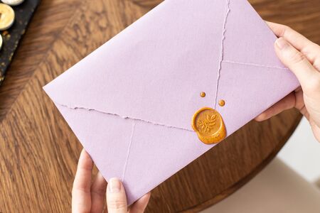 A woman is holding a welcome envelope with a wax seal, a gift certificate, a postcard, a wedding invitation. Soft focus. Close-up.の写真素材