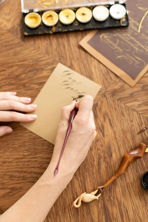 Attractive woman calligrapher is holding a pen with ink and signs a card in handwritten font. Close-up. Soft focus.の写真素材