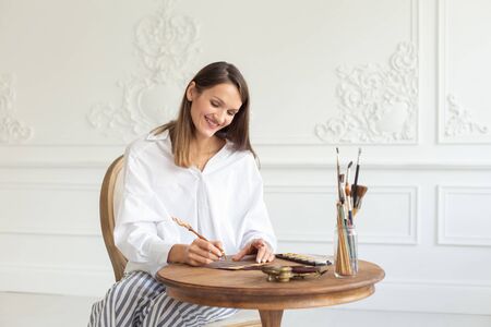 Young beautiful smiling calligrapher girl working in a workshop on a new project. Bright creative studio with sunlight. Soft focus.の写真素材