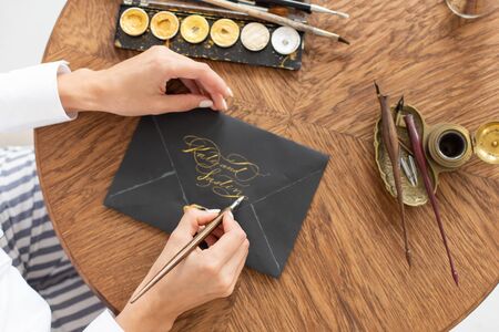 Woman calligrapher is holding a pen with ink and signs a letter in handwritten font. Close-up. Soft focus. Top view.の写真素材
