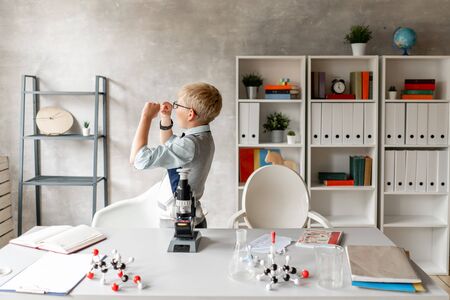 Schoolboy in glasses looks at sample on glass at chemistry lessonの写真素材